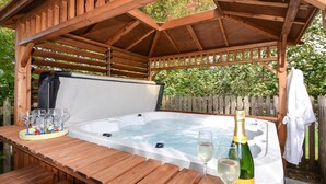 A wooden gazebo with a hot tub, a table with glasses and a bottle, and a fence in the background. - 2 Bed in Truro (oc-ljasm) (Tregavethan)