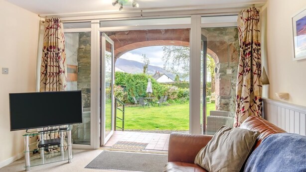Ein Wohnzimmer mit Fernseher, einer Couch und Blick auf einen Garten durch eine Glastür.