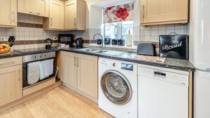 Eine moderne Küche mit Holzausstattung, einer Waschmaschine, einem Kühlschrank und einem Fenster mit Blick auf Blumen.