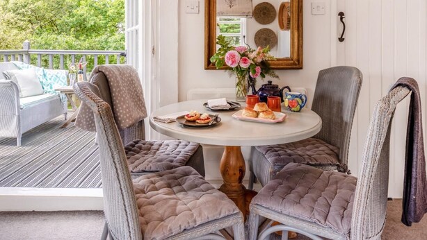 A dining area with a round table, cushioned chairs, a mirror, and a view of the outdoors. - 2 Bed in Holsworthy (oc-32154) (North Tamerton)