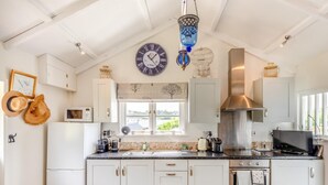 A modern kitchen with white cabinets, a stainless steel range hood, a microwave, and a large window. - 2 Bed in Holsworthy (oc-32154) (North Tamerton)