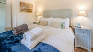 A neatly made bed with white and blue bedding, two bedside lamps, a small bedside table with a lamp, and a framed picture on the wall. - 2 Bed in Holsworthy (oc-32154) (North Tamerton)