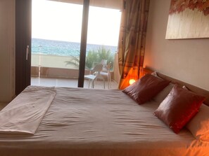 Una camera da letto con un letto, un comodino, una lampada e vista sul mare da una porta finestra.