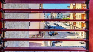 Blick durch ein Fenster mit Querstreben, der eine Straßenszene mit Gebäuden und parkenden Autos zeigt.