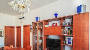 Ein Essbereich mit Holztisch und -stühlen, einer Kristallleuchtre und einem Fernseher auf einem Holzschrank.