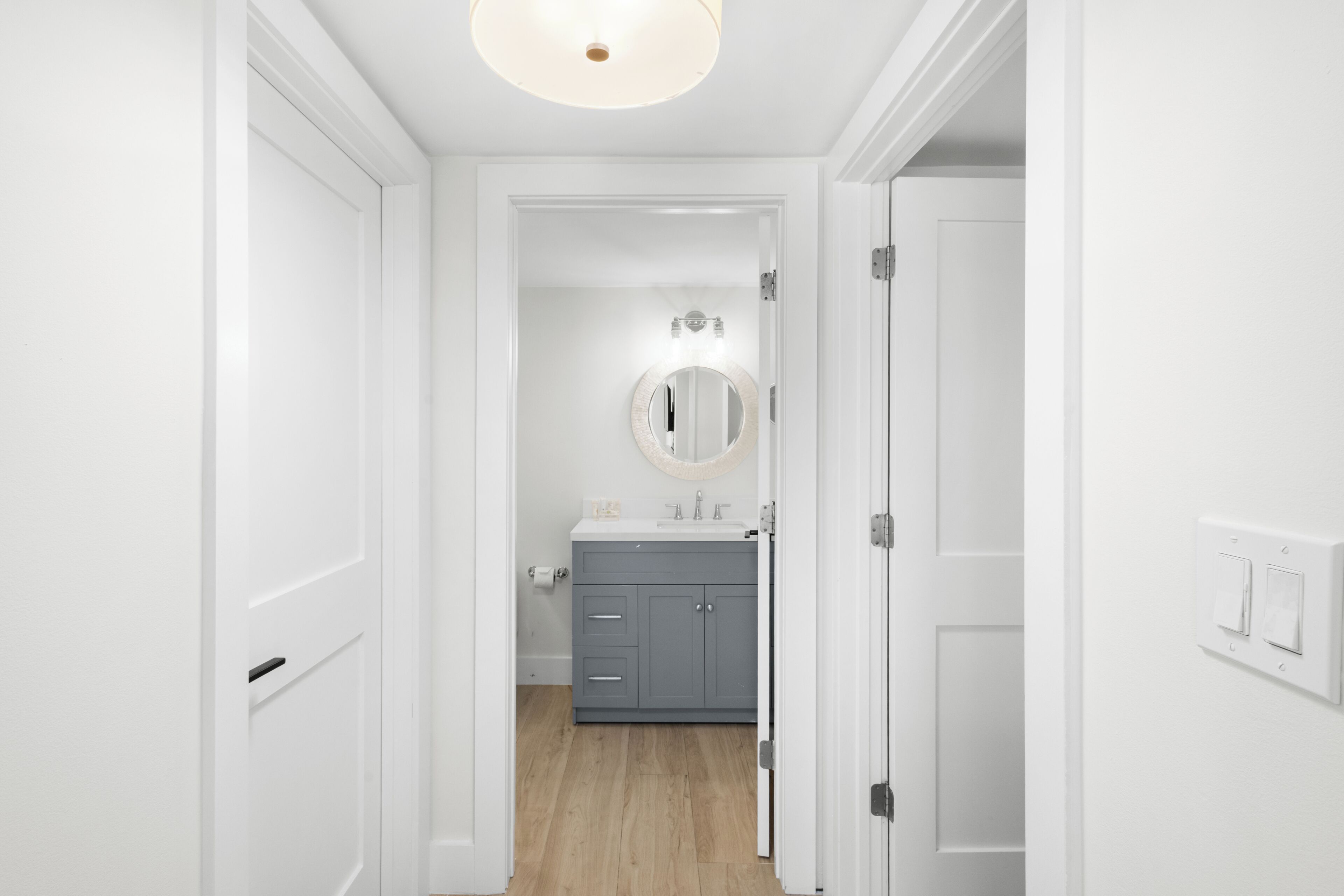 A hallway leading to a bathroom with a sink and mirror.