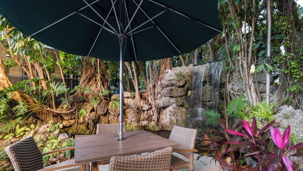 A dining area with a table and chairs, surrounded by lush greenery and a waterfall feature. - Signature Luxury 2/2 Condo Retreat (Miami)