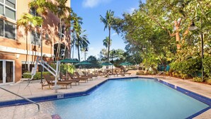 A swimming pool with lounge chairs, palm trees, and a building with a tiled pool edge. - Signature Luxury 2/2 Condo Retreat (Miami)
