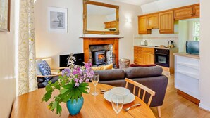 Ein Wohnzimmer mit Kamin, einem Esstisch mit Blumenvase, einer Couch und einer Küche mit Holdekor und Herd.