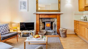 A living room with a fireplace, a television, a sofa, and a dining table with a bowl of fruit.