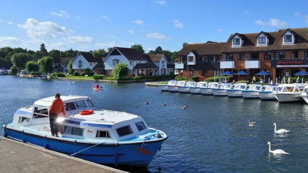 A riverside view with a docked boat, a row of houses, and a restaurant. - 2 Bed in North Walsham (oc-29570) (Worstead)