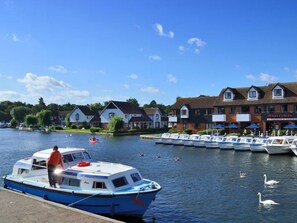 A riverside view with a docked boat, a row of houses, and a restaurant. - 2 Bed in North Walsham (oc-29570) (Worstead)