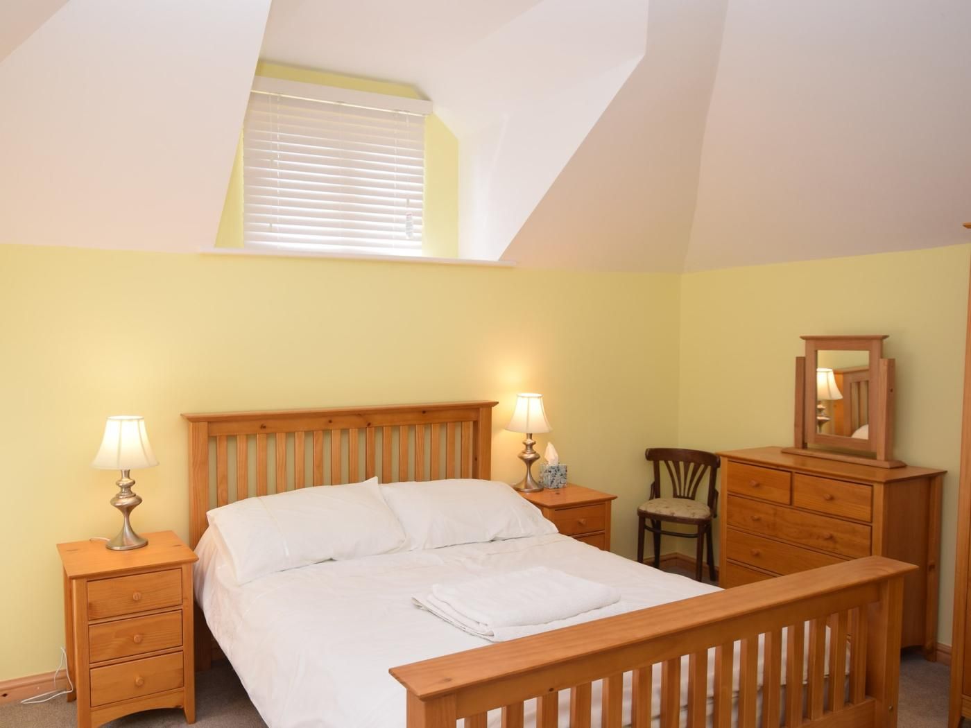 A bedroom with a wooden bed, two bedside tables with lamps, a chair, a dresser, and a mirror.