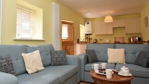 A cozy living area with a sofa set, a small table with a teapot and cups, and a kitchen area in the background. - 2 Bed in North Walsham (oc-29570) (Worstead)