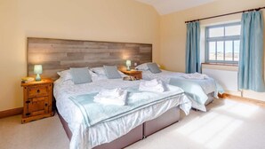Un dormitorio con dos camas, cabeceros de madera, mesitas de noche con lámparas, una ventana con cortinas y un radiador.