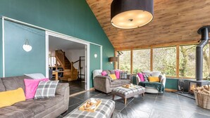 A spacious living room with a high ceiling, a fireplace, and large windows. - 3 Bed in Holsworthy (oc-29125) (Thornbury)