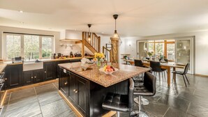 A spacious kitchen with a central island, dark cabinetry, and a dining area with a wooden table and chairs. - 3 Bed in Holsworthy (oc-29125) (Thornbury)