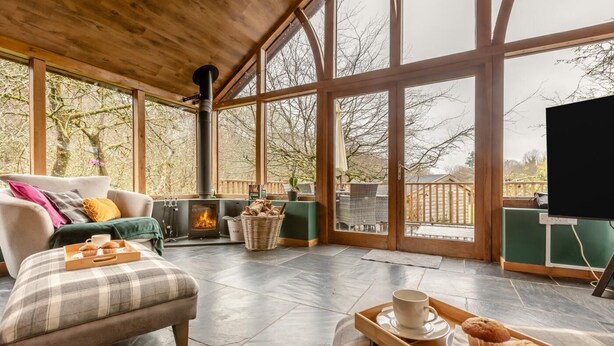 A cozy room with a fireplace, a sofa, a dining table with pastries, and large windows. - 3 Bed in Holsworthy (oc-29125) (Thornbury)