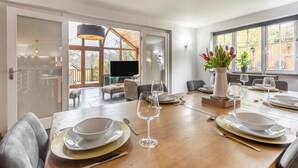 A dining area with a wooden table set for four, a television, and a view of the outdoors. - 3 Bed in Holsworthy (oc-29125) (Thornbury)
