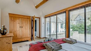 A bedroom with a bed, a wooden wardrobe, a large window with blinds, and a view of the outside. - 1 Bed in Lechlade (oc-31912) (Lechlade)