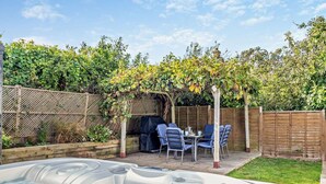 Un jardin avec un jacuzzi, une clôture en bois et une pergola recouverte de plantes grimpantes.