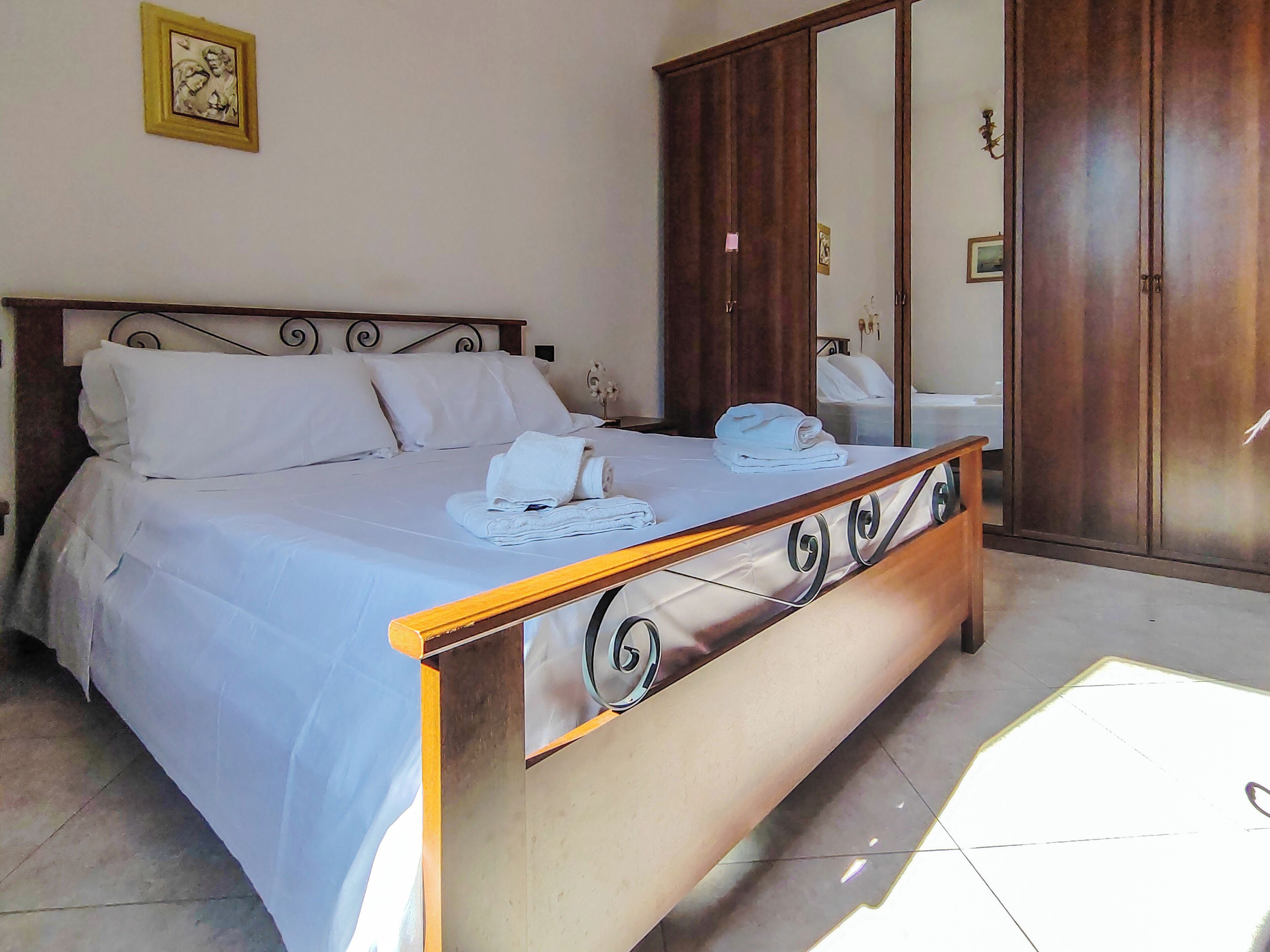A neatly made bed with white linens, a wooden headboard, and a mirror cabinet with a door.