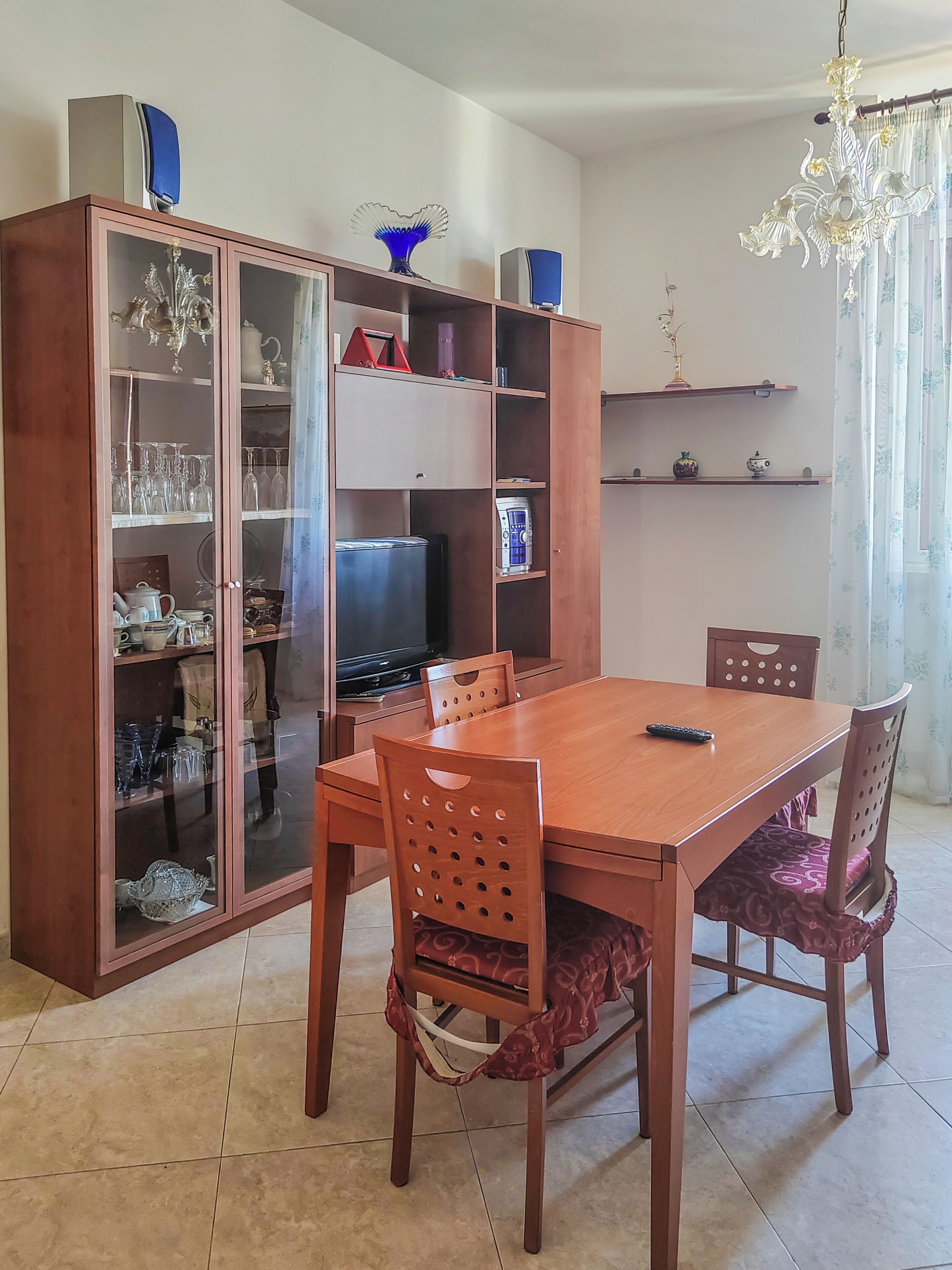 A dining area with a wooden table and chairs, a cabinet with glass doors, and a television.
