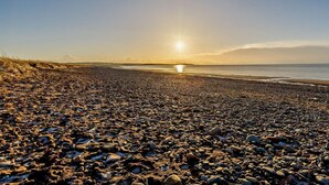 En strand med sten og sand, en klar himmel og solnedgang eller solopgang.