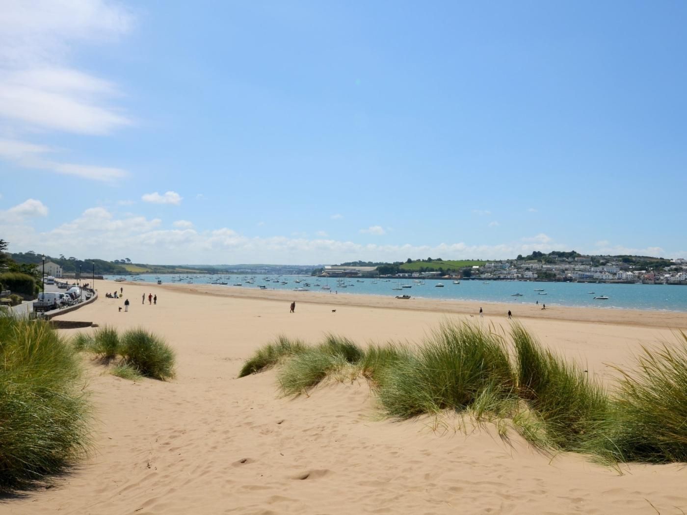 A sandy beach with boats in the water, a clear sky, and buildings in the distance.