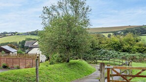 A rural landscape with a wooden gate, a pathway, and a large tree. - 2 Bed in Barnstaple (oc-28959) (Newton Tracey)