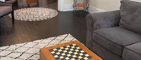 A living room with a pool table, a sofa, a TV mounted on the wall, and a chessboard on a table.