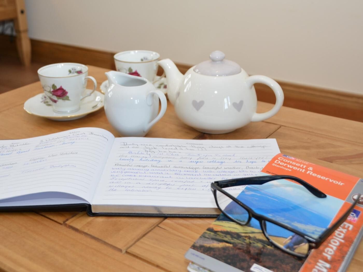 Ein Tisch mit einem Notizbuch, einem Teekessel, Tassen und einem Buch.