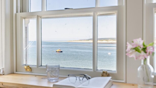 Una vista attraverso una finestra: un libro, occhiali e un bicchiere d'acqua su un ripiano di legno.