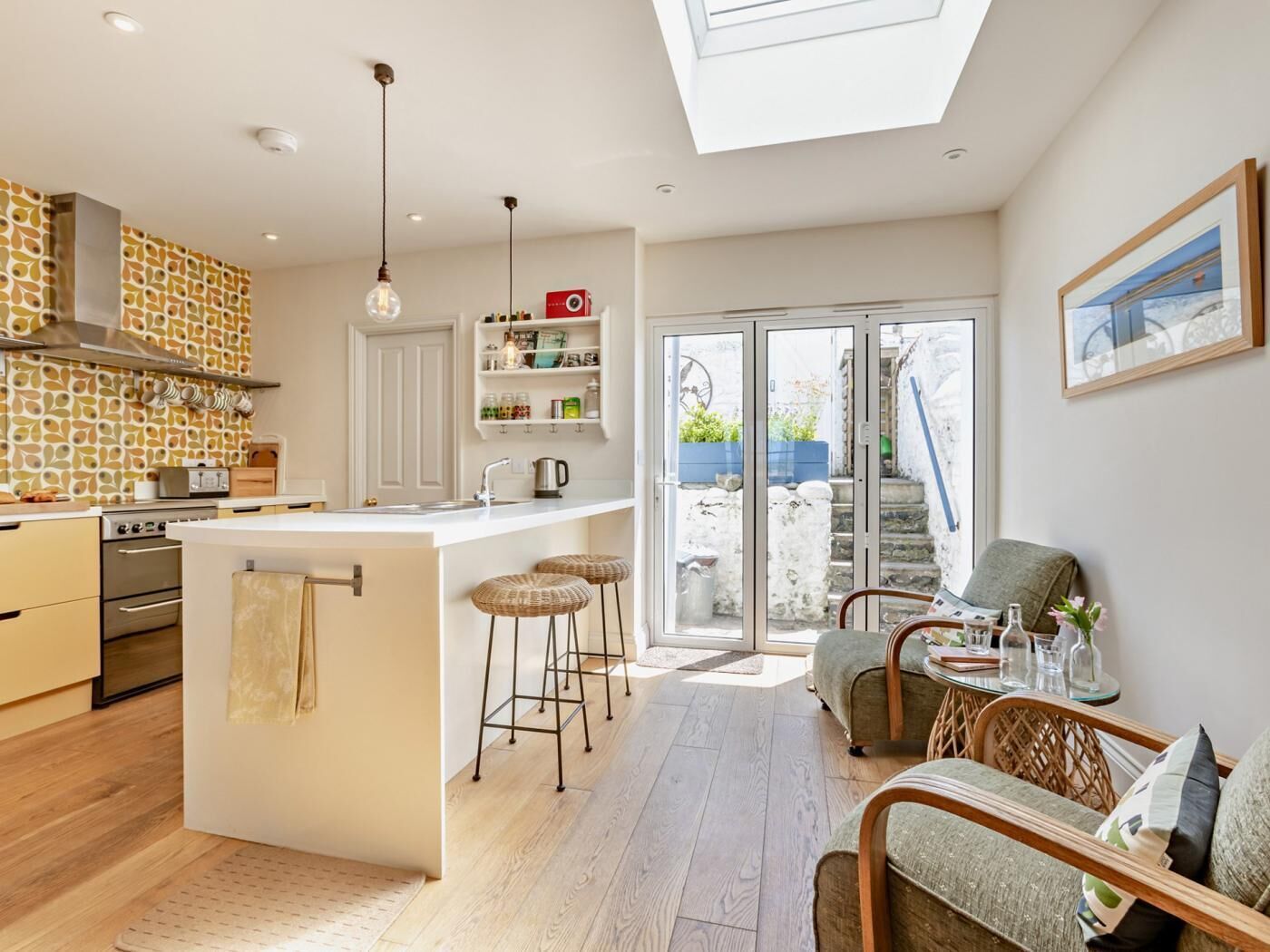 A modern kitchen with a central island, wooden flooring, and a skylight.