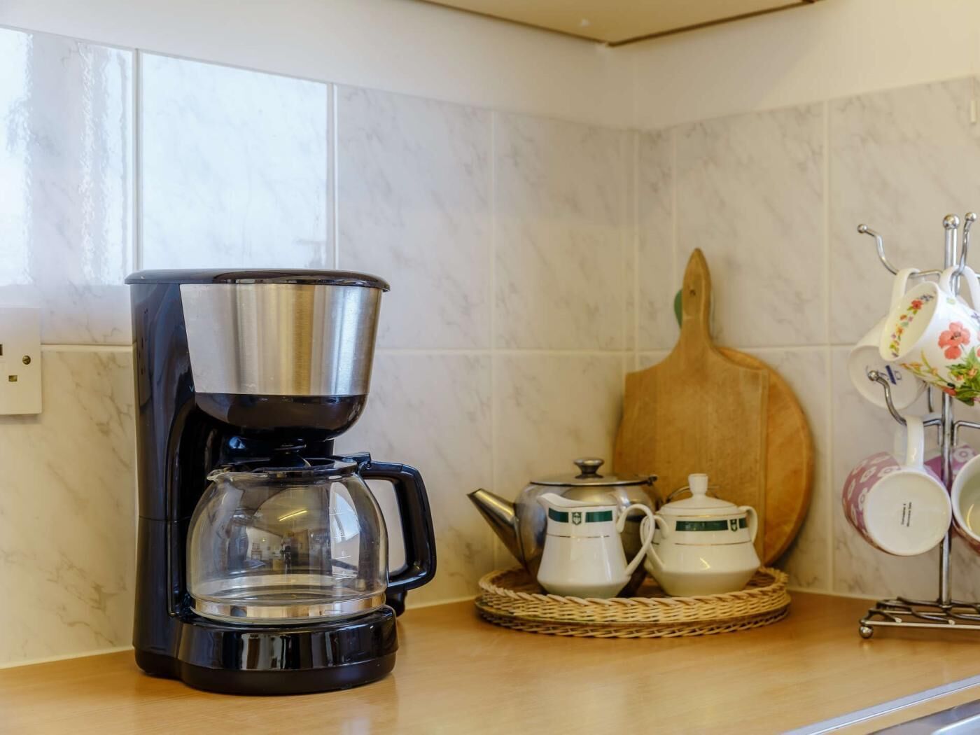 A kitchen with a coffee maker, teapot, cups, and a wooden board.