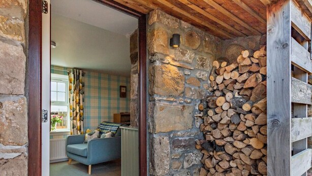 A stone wall with a stack of firewood and a wooden structure to the right. - 1 Bed in Forres (oc-32129) (Alves)