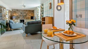 A modern living room with a stone wall, a sofa, a dining table with a glass top, and a television. - 1 Bed in Forres (oc-32129) (Alves)