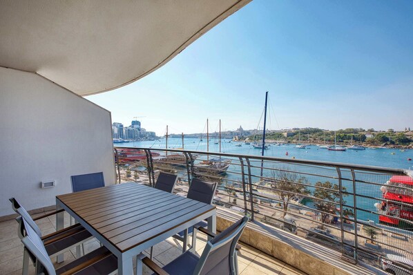 Un balcón con mesa y sillas, con vistas a un puerto deportivo con barcos y un paisaje urbano al fondo.