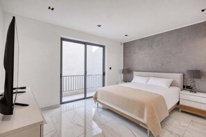 Un dormitorio moderno con cama, mesitas de noche, televisor y puerta corrediza al balcón.