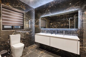 Un baño moderno con inodoro blanco, un espejo grande y un tocador blanco con ducha.