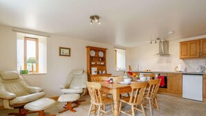 A dining area with a wooden table and chairs, a leather chair, a cabinet with dishes, and a kitchen in the background. - 2 Bed in Middlesbrough (oc-tgchf) (Chop Gate)