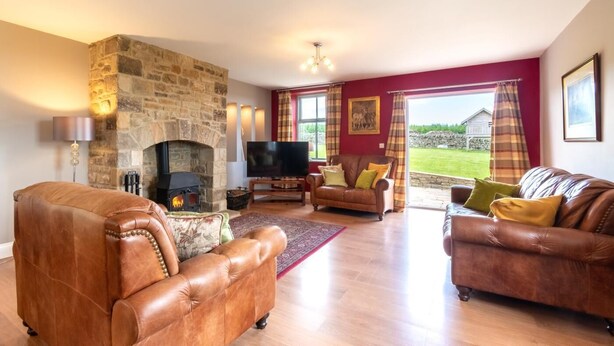 A living room with leather sofas, a stone fireplace, a TV, and a view of the outdoors. - 3 Bed in Consett (oc-29408) (Lanchester)