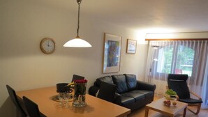 A living room with a dining table, a sofa, a chair, a clock, and a window with curtains. - Hof Arosa A-03 Appartement/Fewo,   4-Bettwohnung by Interhome (Arosa)