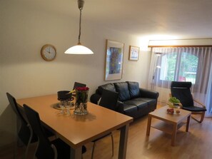 A living room with a dining table, a sofa, a chair, a clock, and a window with curtains. - Hof Arosa A-03 Appartement/Fewo,   4-Bettwohnung by Interhome (Arosa)