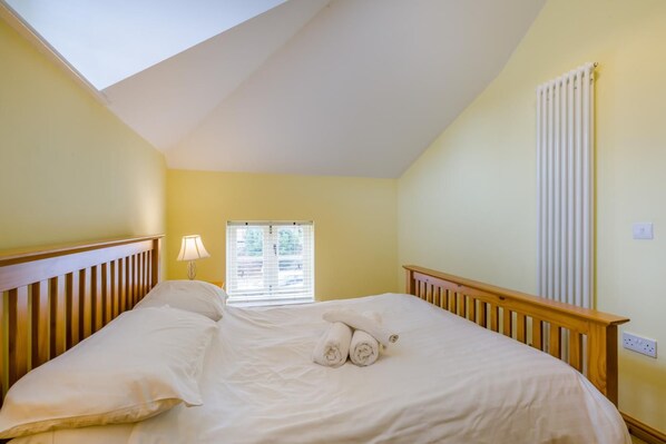 A bedroom with a sloped ceiling, a bed with white linens, a window with blinds, and a radiator.