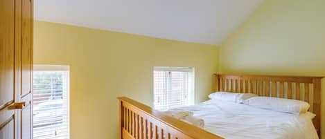 A bedroom with a wooden bed, two windows with blinds, and a wooden wardrobe.