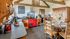 Een rustieke keuken met houten balken, een rode fornuis en een eethoek met een houten tafel en stoelen.