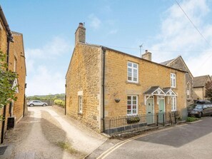 A stone building with a traditional design, a gated driveway, and a clear sky. - 2 Bed in Cheltenham (oc-29027) (Bourton-on-the-Water)
