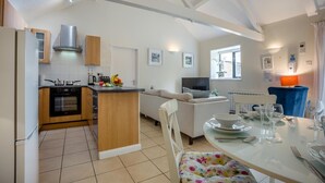 A compact kitchen with modern appliances, a dining area with a table set for two, and a living space with a sofa and TV. - 2 Bed in Shaftesbury (oc-28678) (Sedgehill)