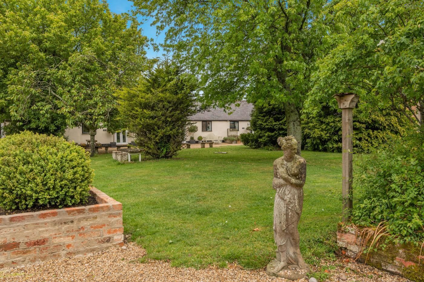 Un jardin avec une statue, un banc et une maison en arrière-plan.